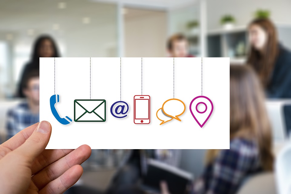 un main tient une feuille sur laquelle apparaissent les logos deu mail, des réseaux sociaux, du web. Derrière se tiennent des personnes du conversent